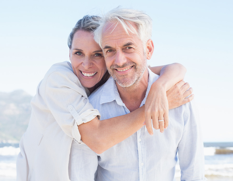 Older couple hugging on Melbourne beach, smiling after receiving financial planning from a financial advisor